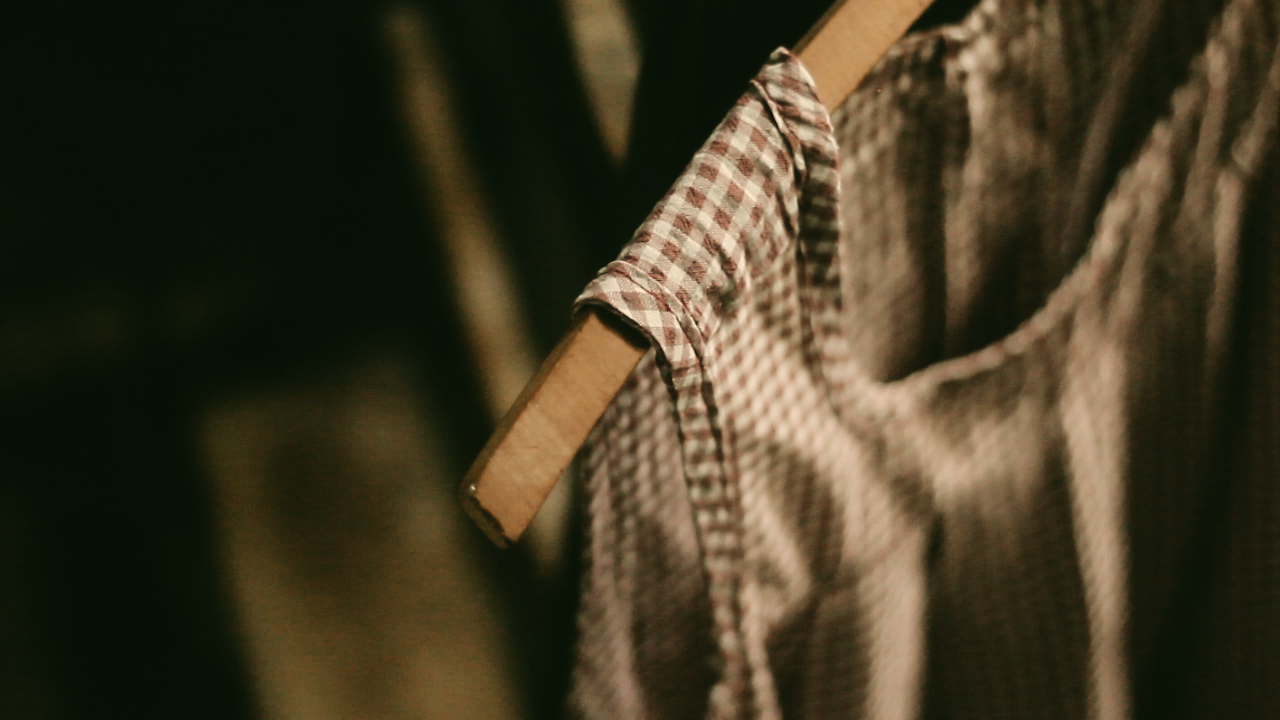 Fotografia. Vestido de algodão listrado em vermelho e branco pendurado em cabide antigo em uma cadeira de madeira.
